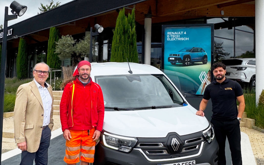 Drei Männer stehen vor dem Autohaus Gutmann mit dem Schriftzug „Gutmann“ neben einem weißen Renault Kangoo E-Tech mit Freiburger Kennzeichen. Einer trägt Anzug, der zweite Arbeitskleidung in Rot-Orange, der dritte ein schwarzes Poloshirt mit Gutmann-Logo. Im Hintergrund ist ein Plakat mit dem Text „Renault 4 E-Tech Elektrisch“ zu sehen.