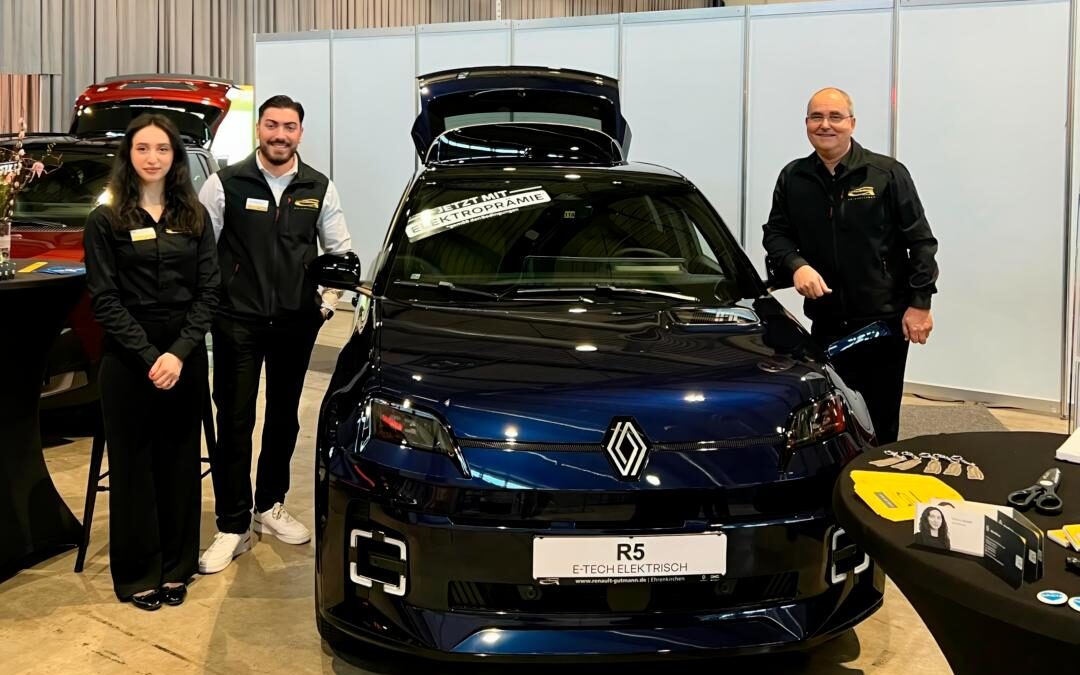 Drei Mitarbeitende des Autohauses präsentieren einen schwarzen Renault R5 E-Tech Electric am Messestand