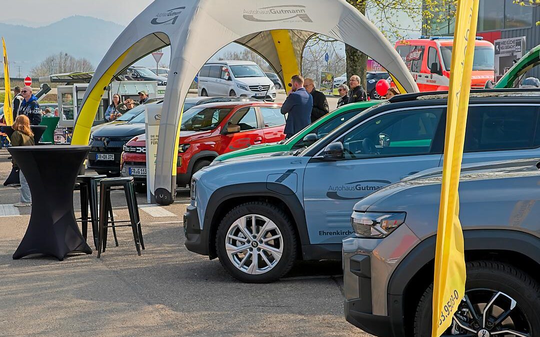 Vor einem blauen R4 E-Tech mit der Aufschrift ‚Autohaus Gutmann – Ehrenkirchen‘ steht ein schwarzer Stehtisch mit Informationsmaterial. Im Hintergrund sind weitere Fahrzeuge und Besucher unter dem Zelt des Autohauses zu sehen.